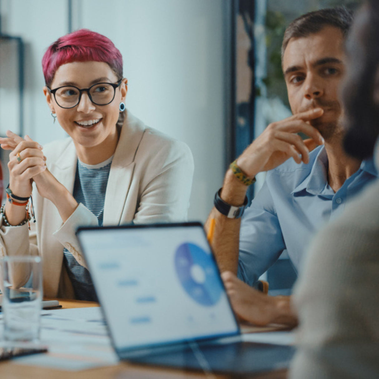 A binary person with a group of people in a meeting with a laptop on a table