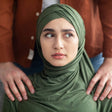 A woman wearing a green hijab feels uncomfortable due to a man's hands on her shoulders