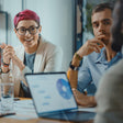 A binary person with a group of people in a meeting with a laptop on a table