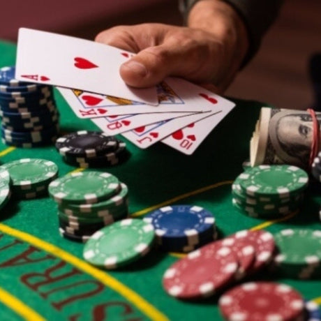 Person holding playing cards with poker chips and money on a casino table
