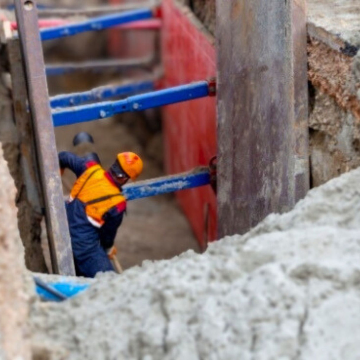 Person in safety gear working on a construction site with concrete and tools.